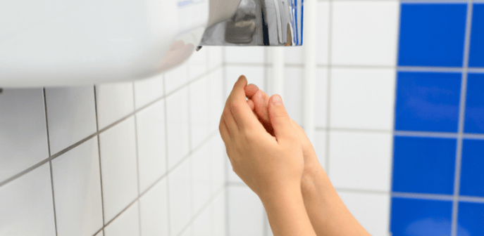 Las manos de una persona usando el secador de manos de un baño